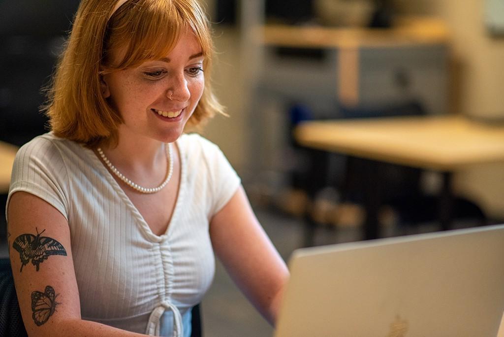 A U N E student sits at a desk and works on a lap top